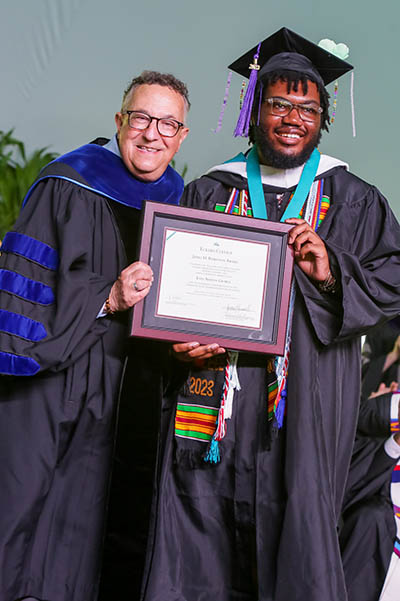 Student in cap and gown and president hold framed certificate