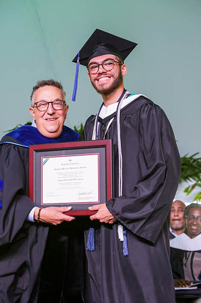 Student in cap and gown and president hold framed certificate