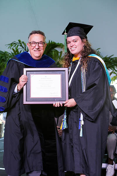 Student in cap and gown and president hold framed certificate