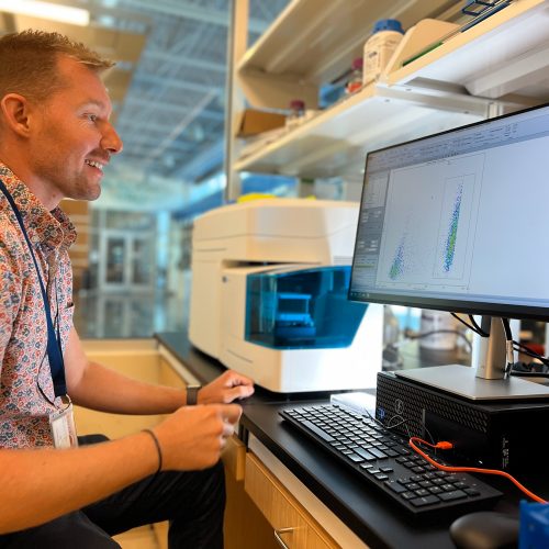 Professor sits at desk with computer and sampling machine