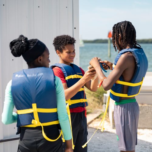Three children helped one another with safety gear near the sailing center at Eckerd College.