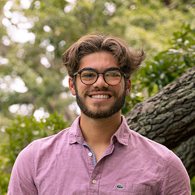 Student in glasses, outdoors, smiles at camera