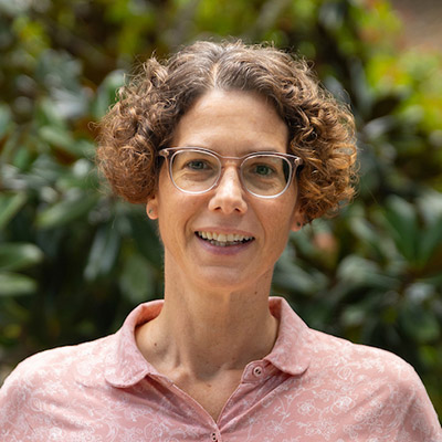 Professor in glasses smiles at camera in outdoor setting