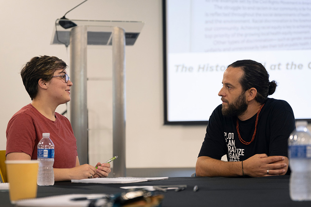 Student speakers with guest speaker while seated at a table with a presentation displayed behind them