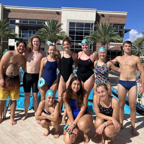 A group of students in swim gear posing in front of a pool