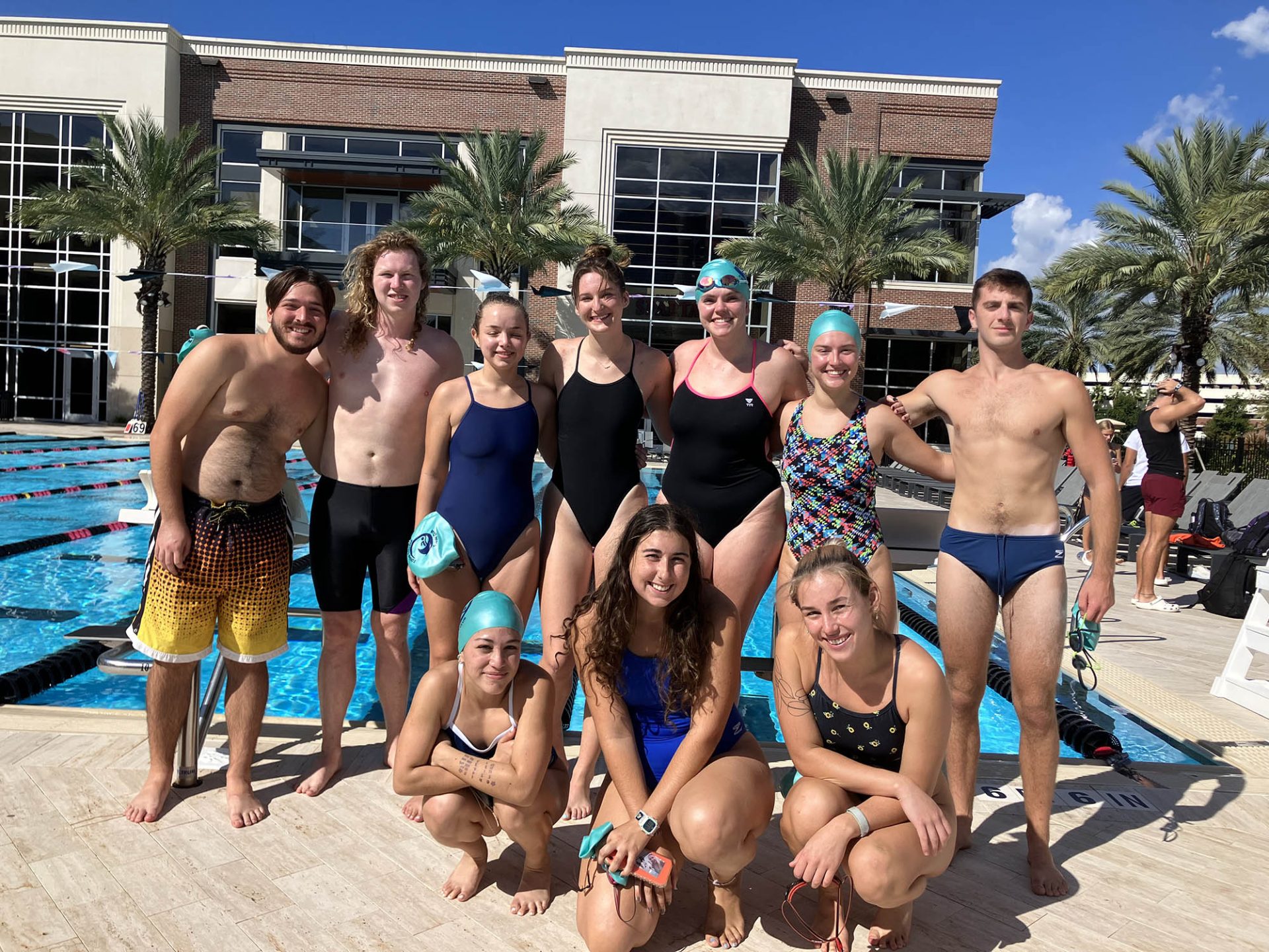 A group of students in swim gear posing in front of a pool