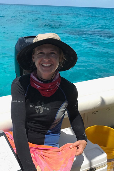 Woman in wet suit seated in a boat with hat and notepad