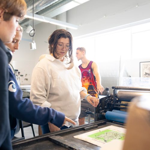 Professor and students leaning over a press