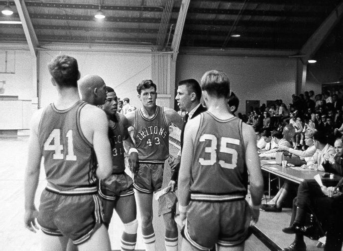 Coach in a huddle of men's basketball players, in black and white