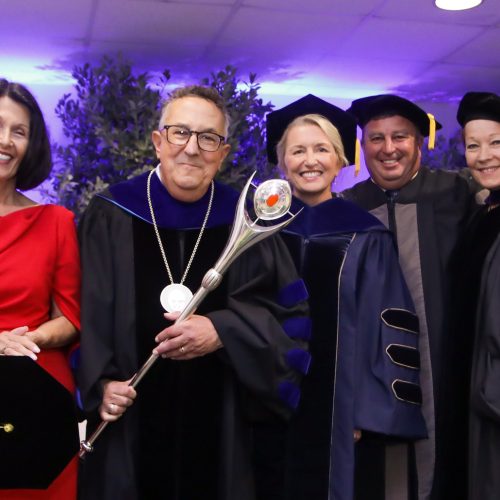 Annarelli holds mace on stage alongside his wife, two trustees and faculty member dressed in regalia