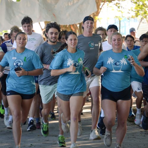 Large group of runners waring teal shirts leaves the starting line