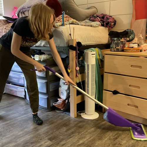 Student uses mop to clean the floor of a dorm room