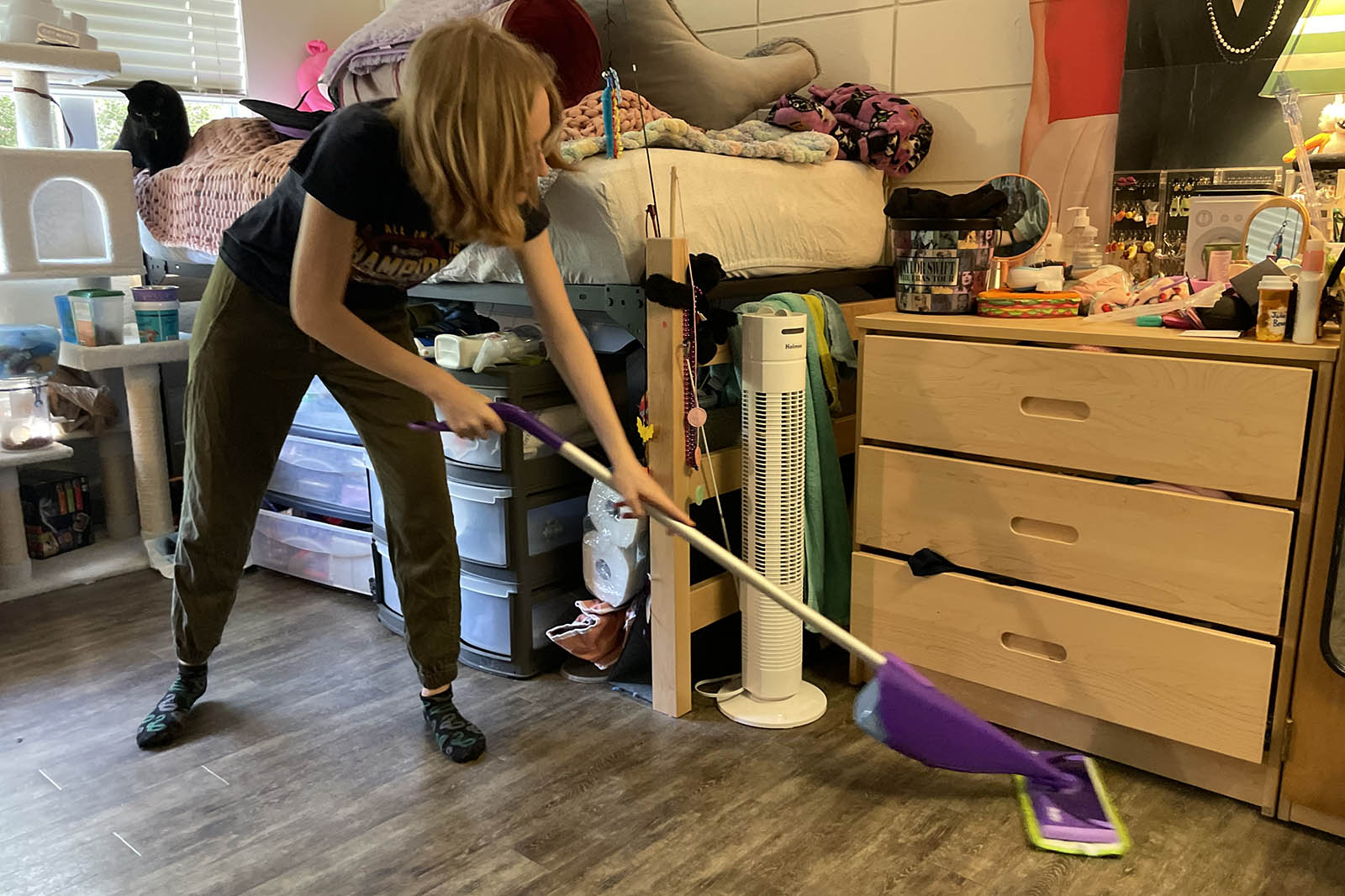 Student uses mop to clean the floor of a dorm room