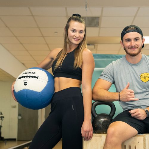 Two student instructors in the fitness center, one holding exercise ball