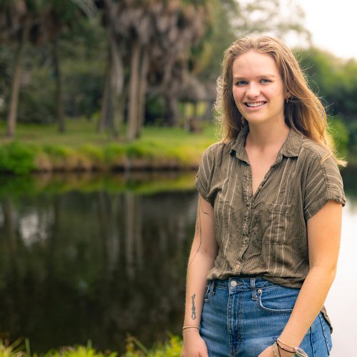 Young woman stands in front of a pond surrounded by palm trees