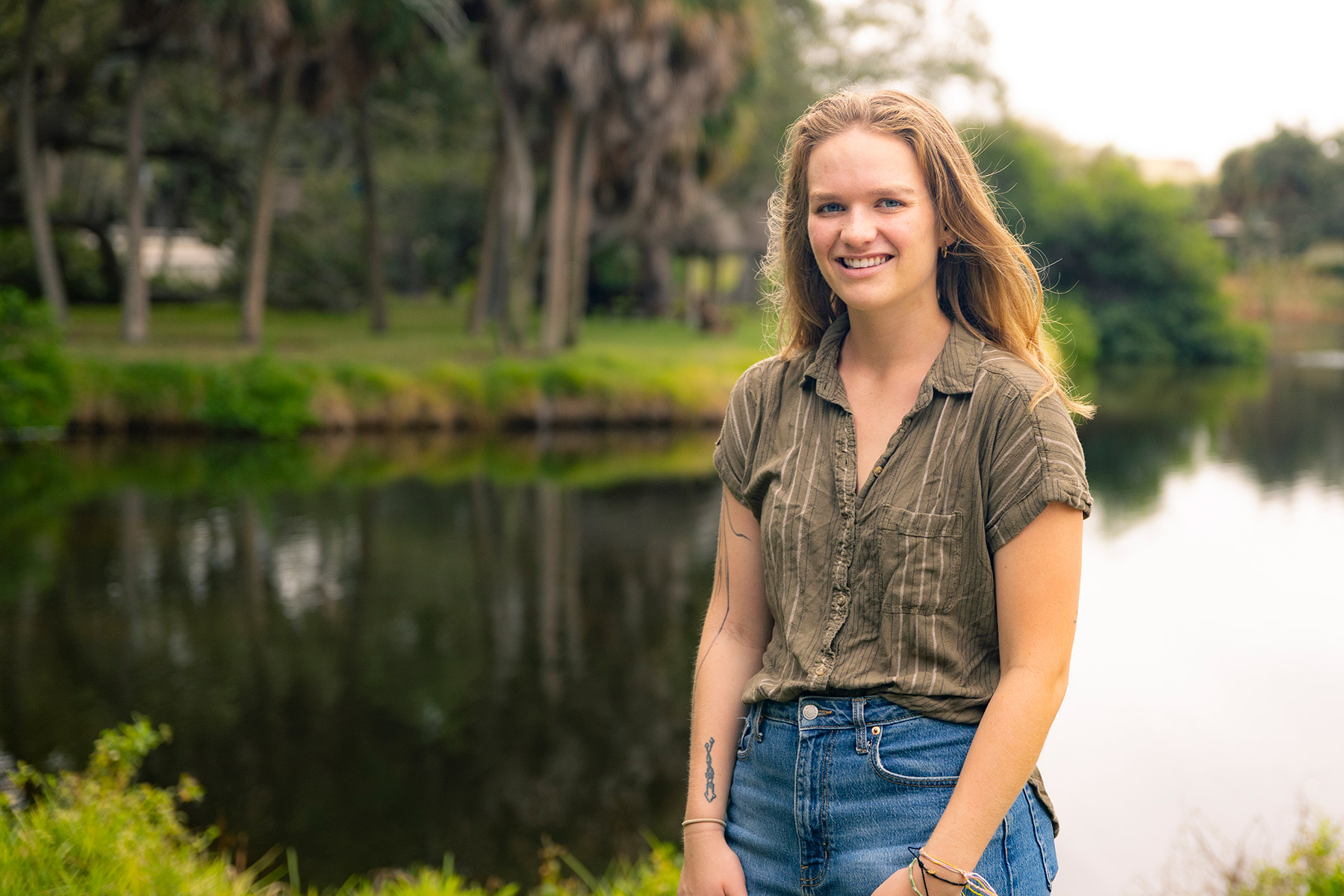 Young woman stands in front of a pond surrounded by palm trees