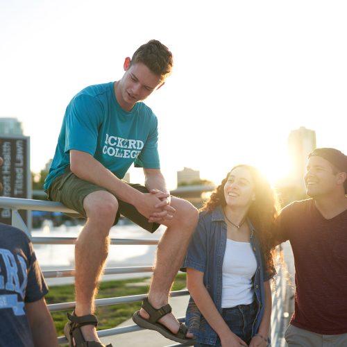 Four Eckerd College students share a laugh along a seaside railing with downtown cityscape in the background