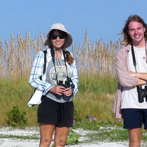 Professor and student wearing binoculars while out in the field in sandy beach area