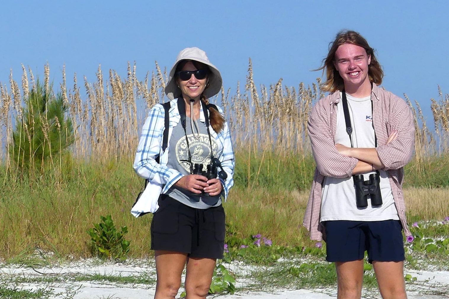 Professor and student wearing binoculars while out in the field in sandy beach area