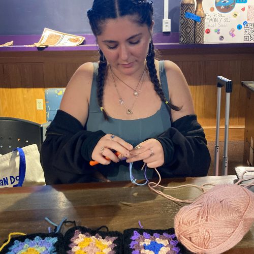 Student in pony tails crochets at a table