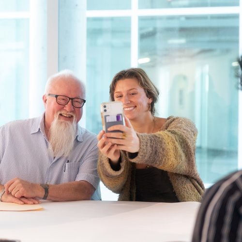 Dr. BBQ at a table with students, one of whom is snapping a selfie with him