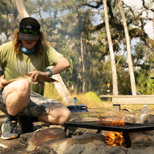 A student prepares wood by a firepit