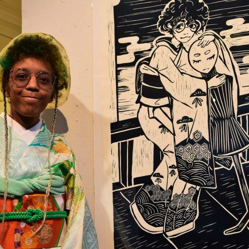 Student in kimono stands next to black and white lino print