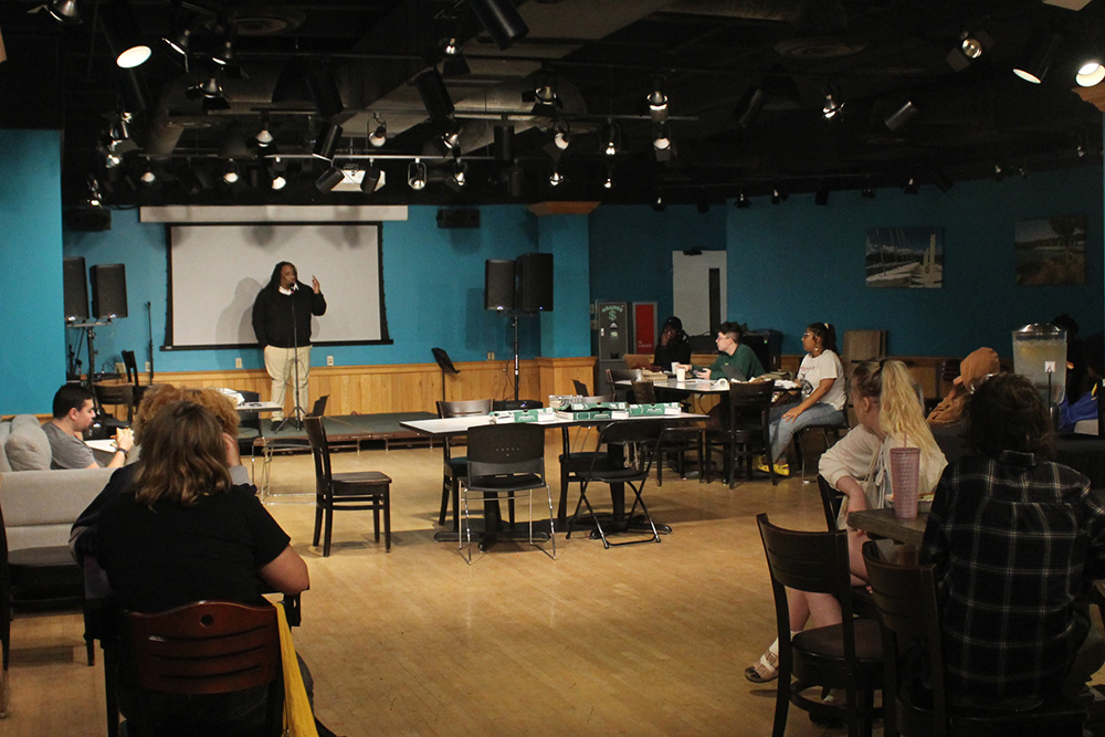 Room with speaker on stage and half a dozen tables with seated students