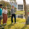 Four students chatting outside under a palm tree by a pond