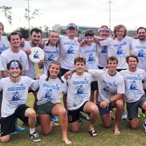 17 students in group huddle, shoulder to shoulder, one holding a disc