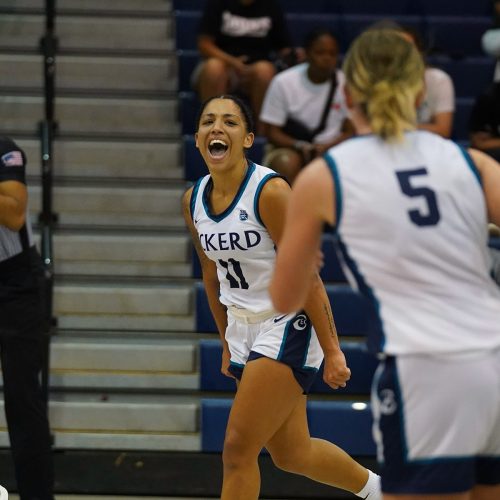 Women's basketball player enthusiastically cheering while jogging down the court