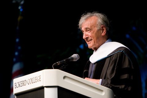 Older man in regalia speaks at podium