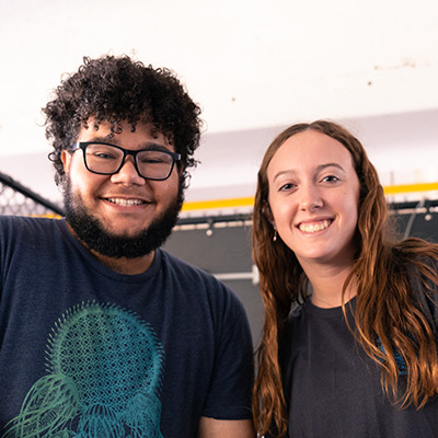 Two students stand side by side, one in glasses and beard