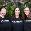 Three women stand side by side on campus with shirts that read "UNTRENDY"