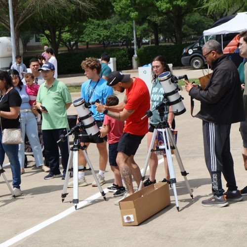 Members of the public use telescopes in a parking lot