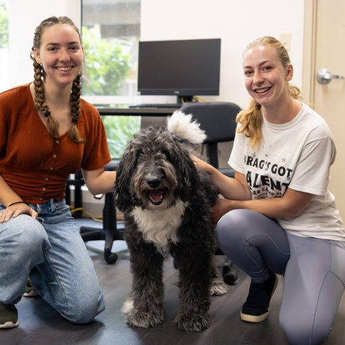 Two students squat with Orlo the dog