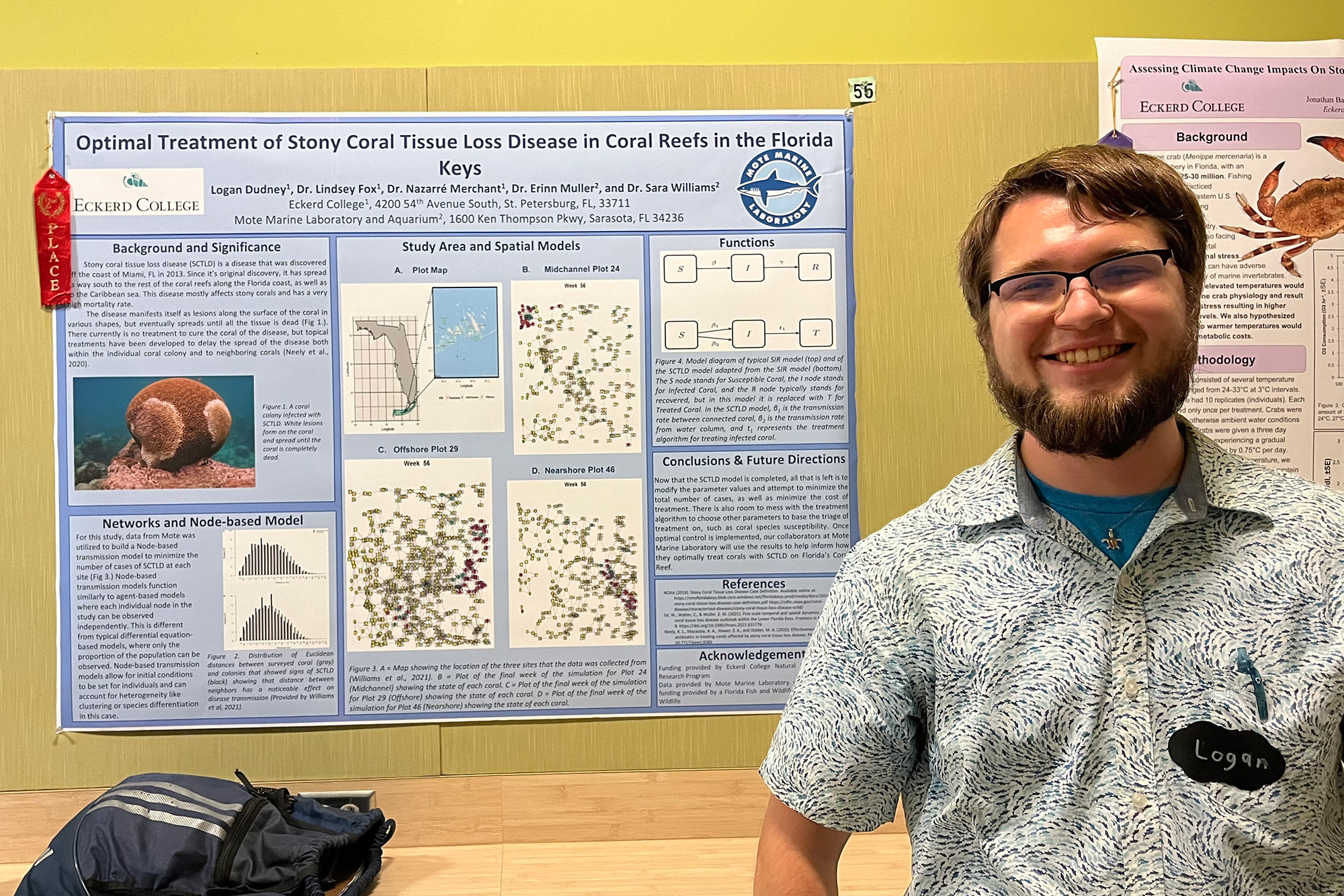Young man with beard stands in front of scientific poster