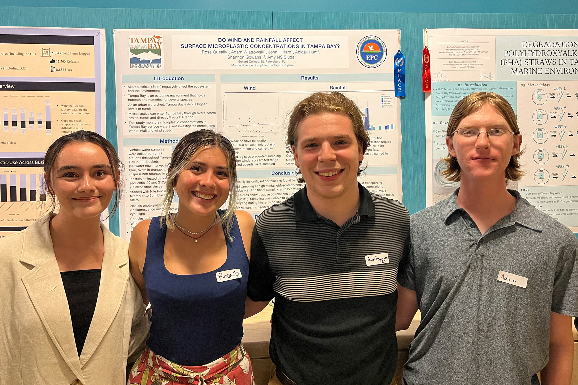 Four students stand side by side in front of a scientific poster