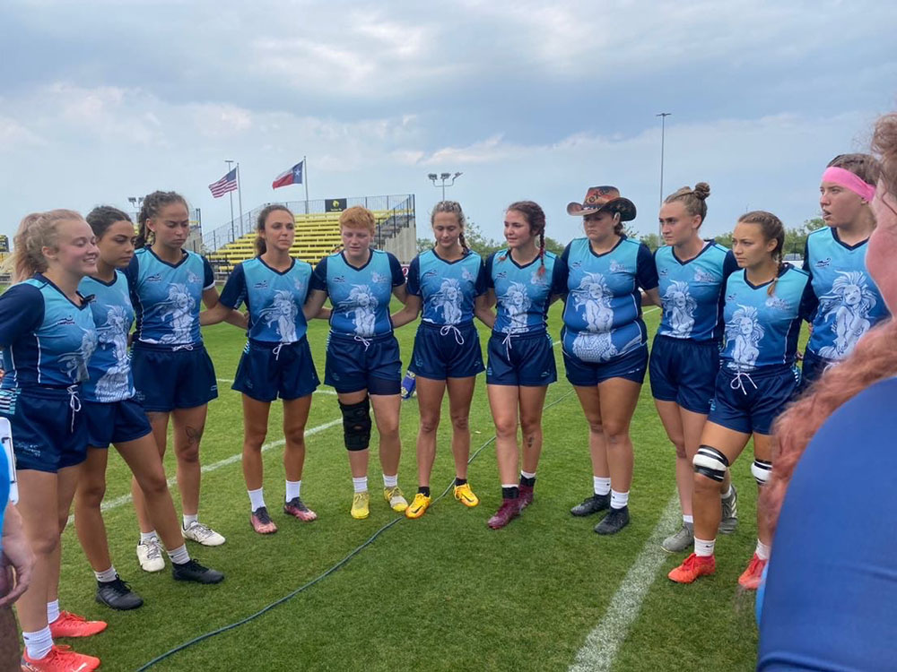 Twelve women's rugby team members wearing the same uniform stand in a circle