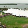 Aerial view of procession of graduates walking in a long line towards a very large tent situated by the water's edge
