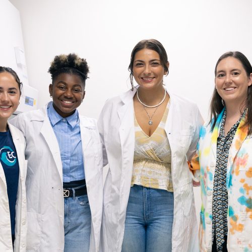 Professor in tie-dye lab coat stands with three students in lab coats