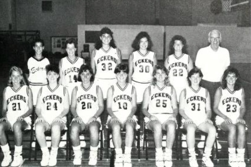 Black and white photo of basketball team players seated next to coach