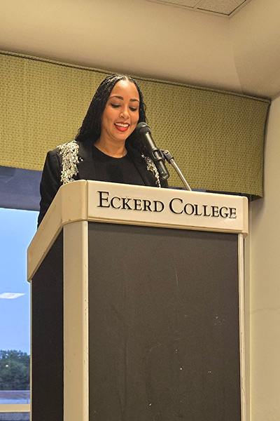 Woman speaks at podium with text "Eckerd College"