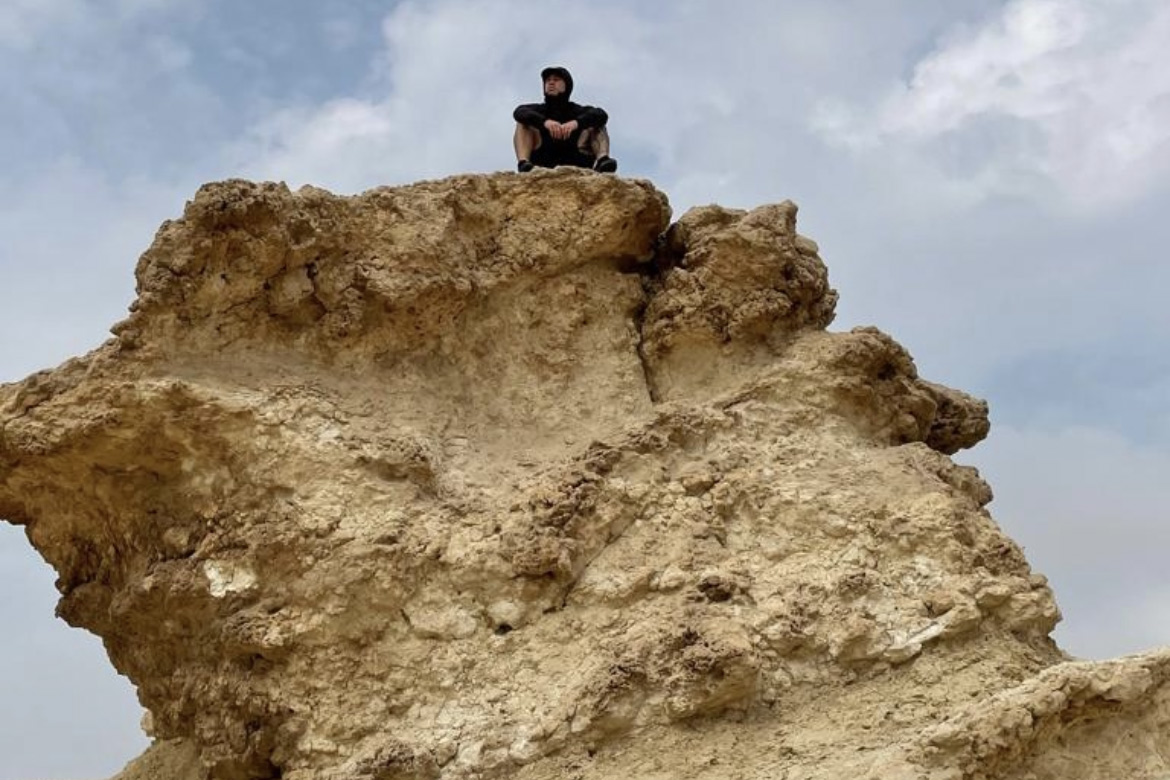 Man sitting atop a large rock in arid landscape
