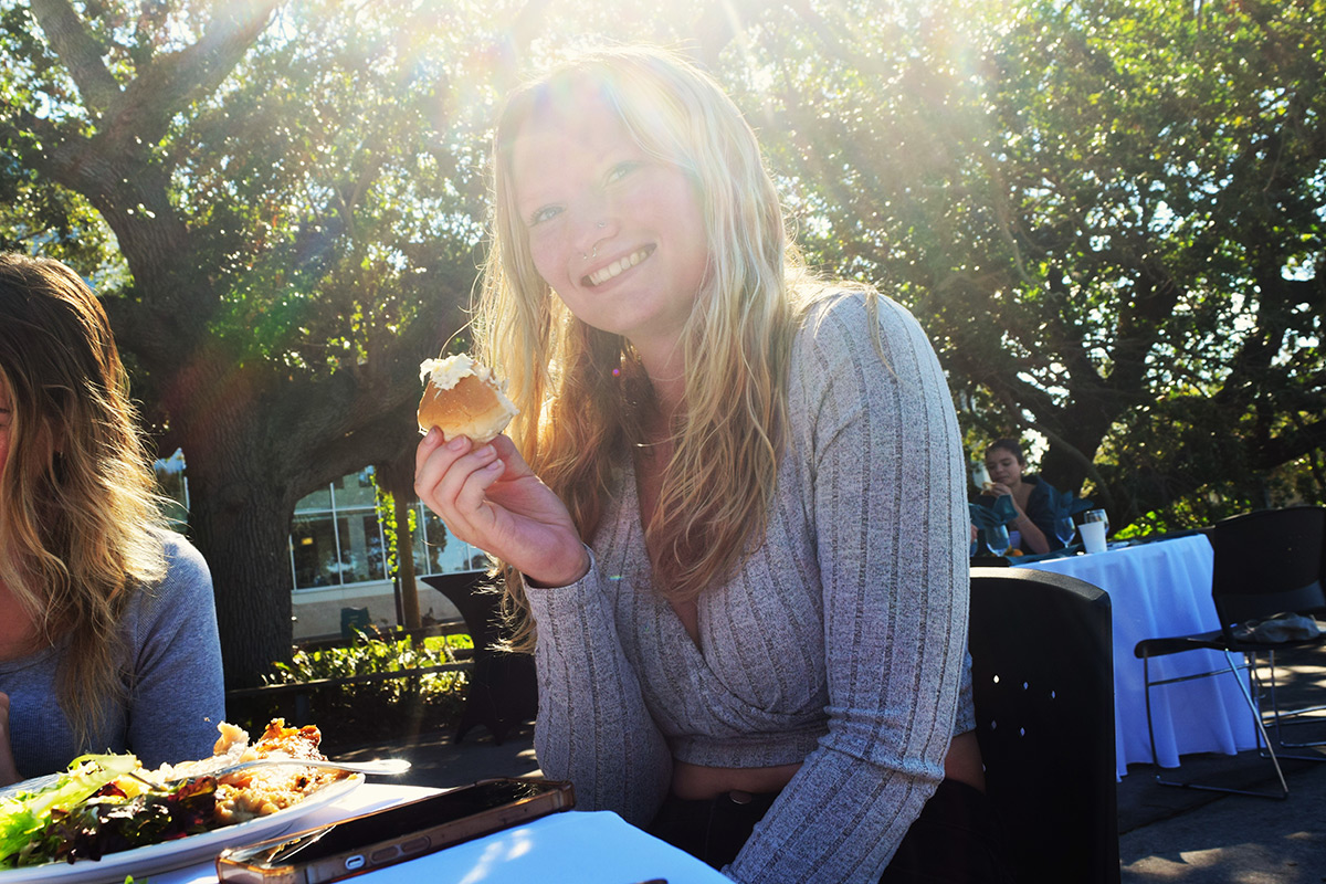 Student seated outside smiles as she eats her meal