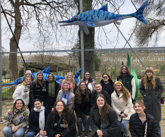 Group of students pose outside under a dolphin statue