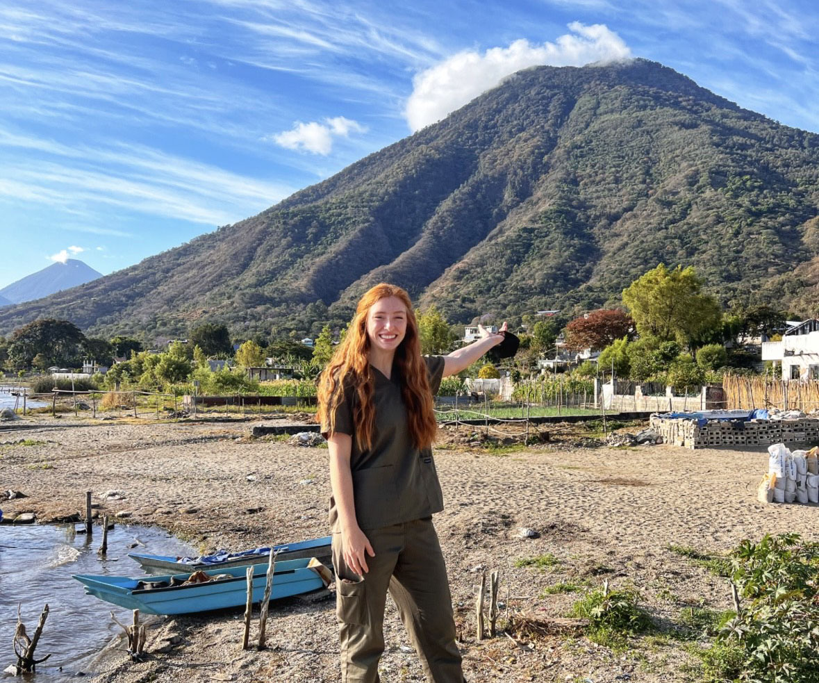 Student stands on small beach on island with volcano in background