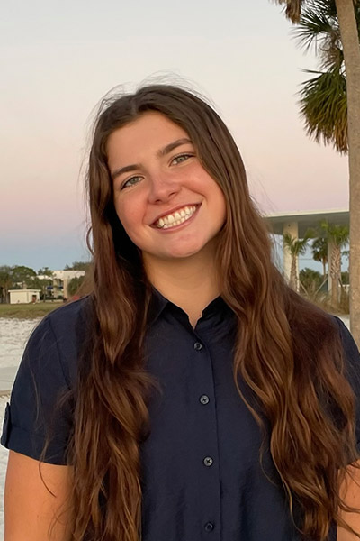 Smiling student stands next to palm tree