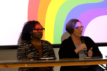 Two panelists sit at a table, one with microphone