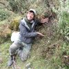 Young man leans against plant-covered hill with hands around a small plant